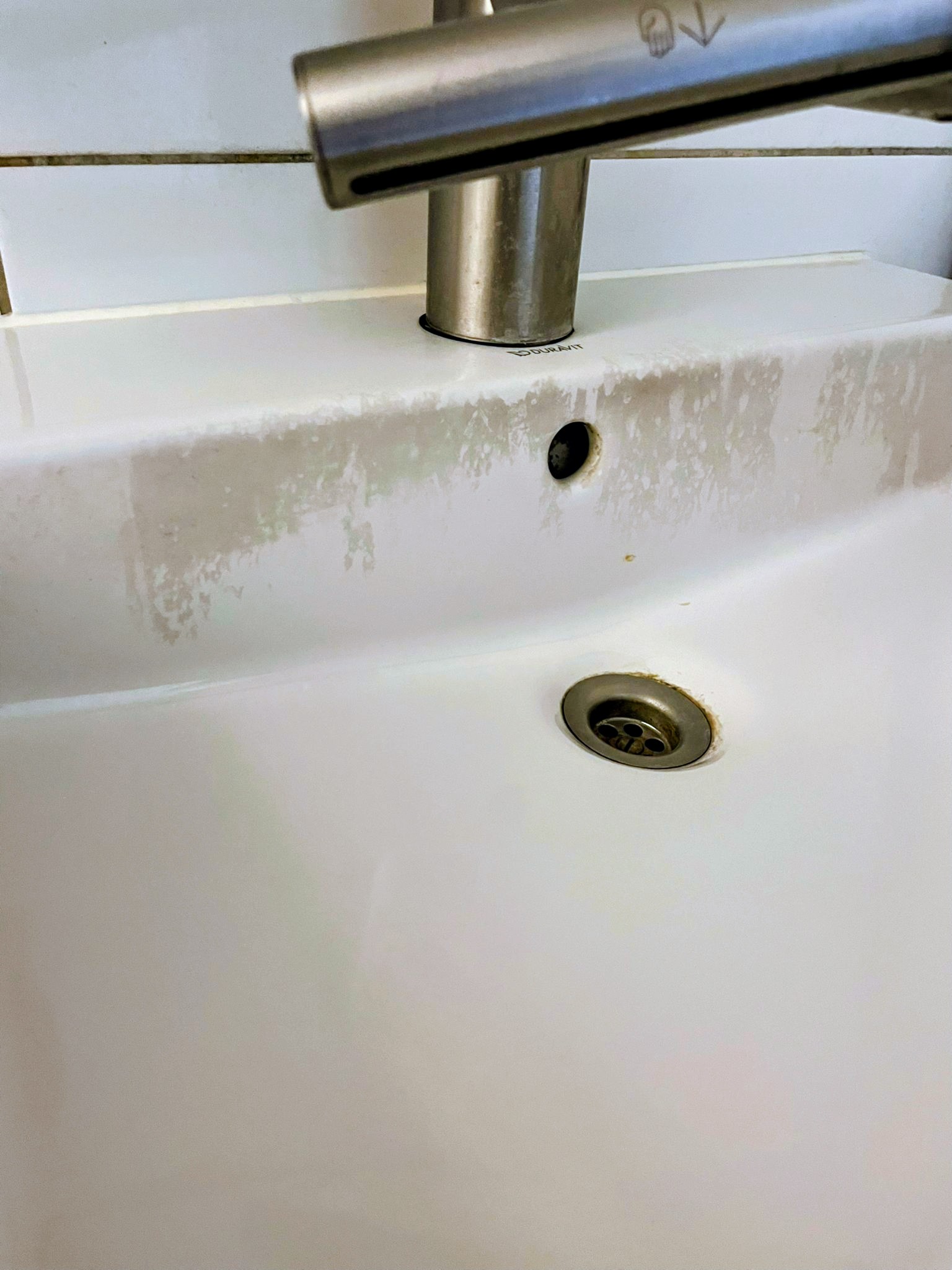 Wastafel met kalkaanslag en vuil rond de afvoer, vóór de schoonmaak